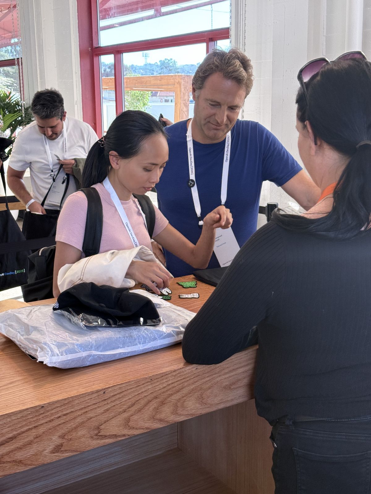 Guests at a wooden counter choosing embroidered patches beside a hat and tote bags